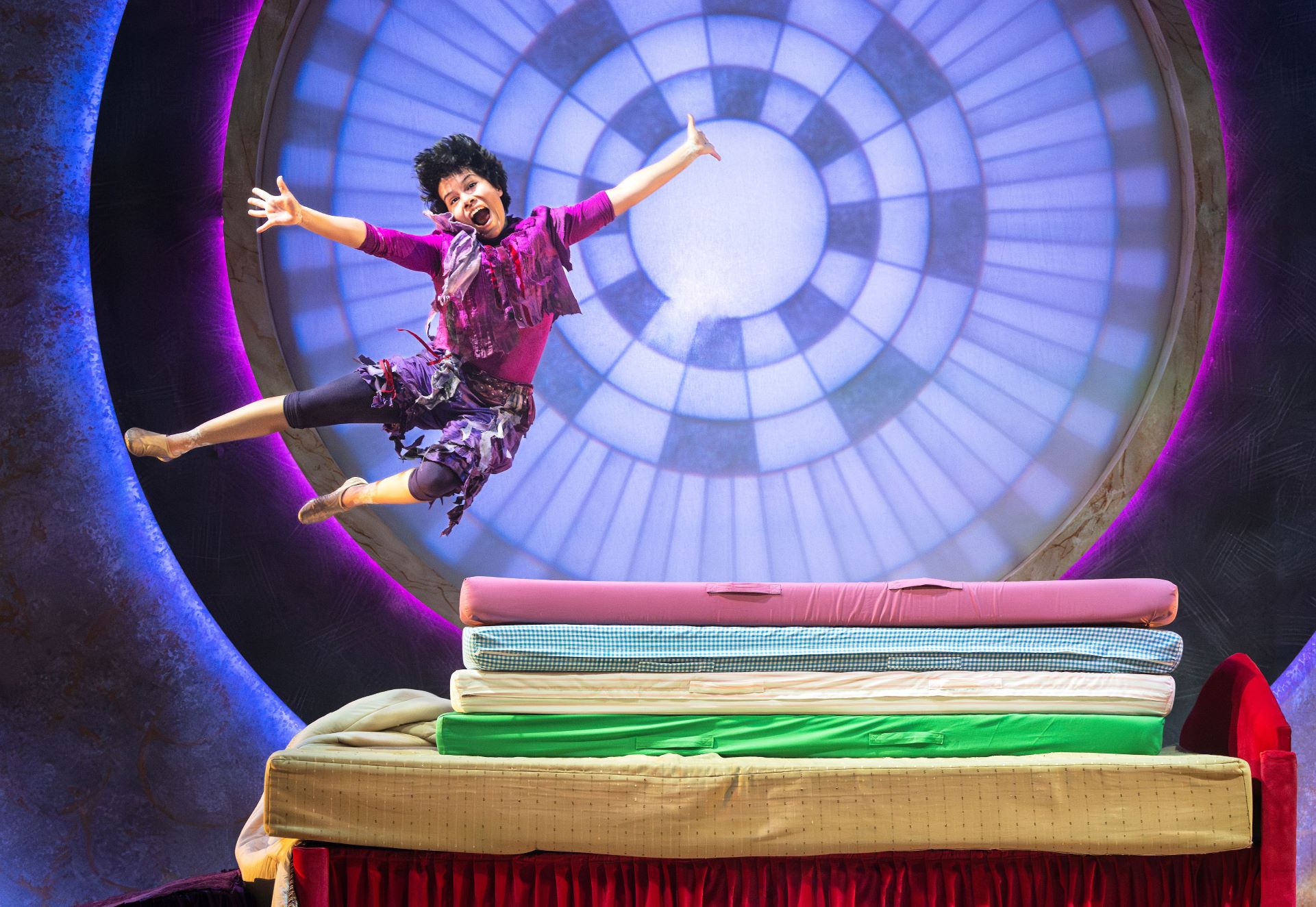 Photo of he Purple Princess from The Princess and the Pea jumping onto a stack of 5 mattresses.