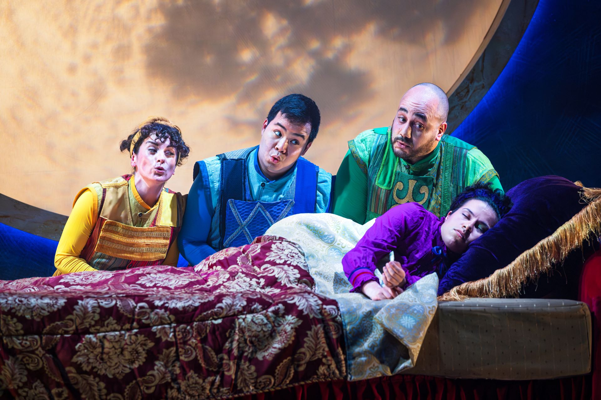 Photo of the cast of The Princess and the Pea where the Yellow, Blue, and Green Servant from left to right sing the Princess Princess to sleep.