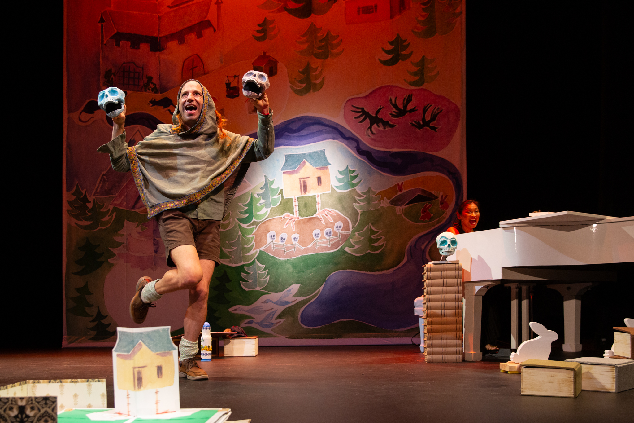 Anton Dudley dances on stage dressed as the Baba Yaga holding two skull puppets