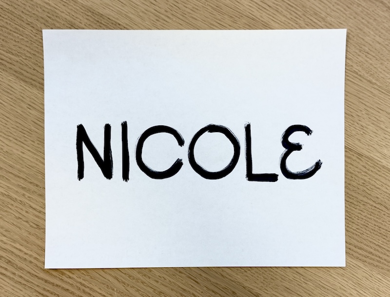 The name NICOLE written in bold black marker on a sheet of paper