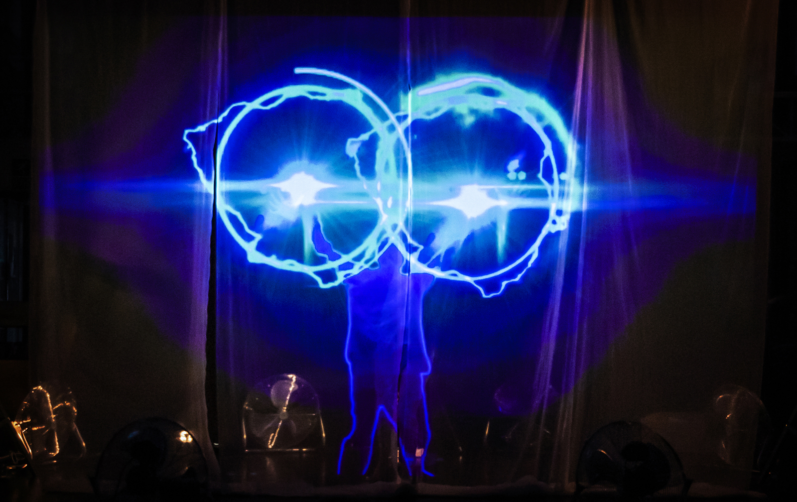 Two large projected blue circular lights with a glowing blue outline of a body behind them.