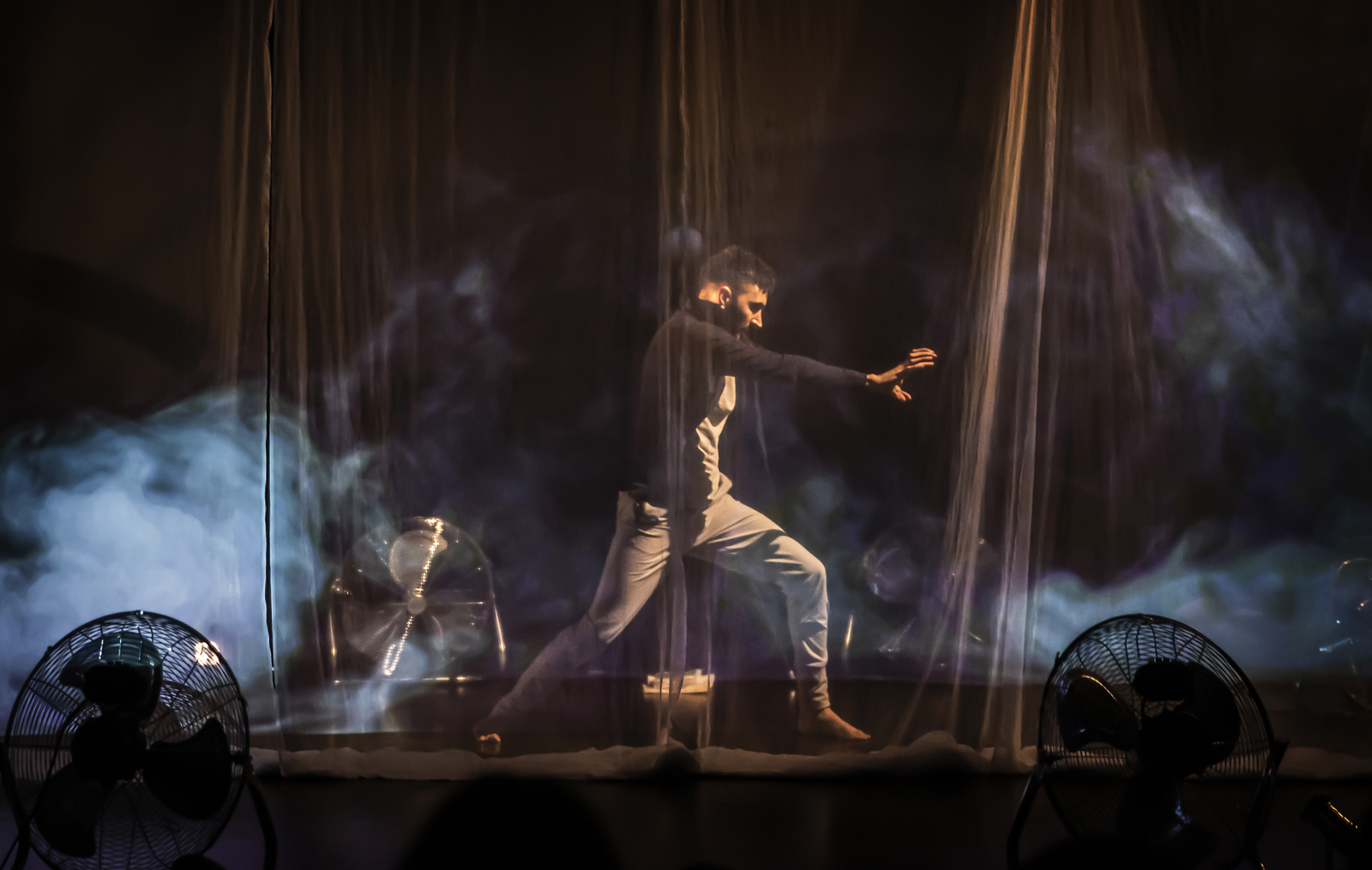 A male-presenting dancer behind a sheer curtain that is moving projected wind.