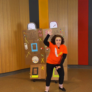 Looping GIF of Siobhan darting behind a homemade cardboard time machine. Her older self emerges from the other side!