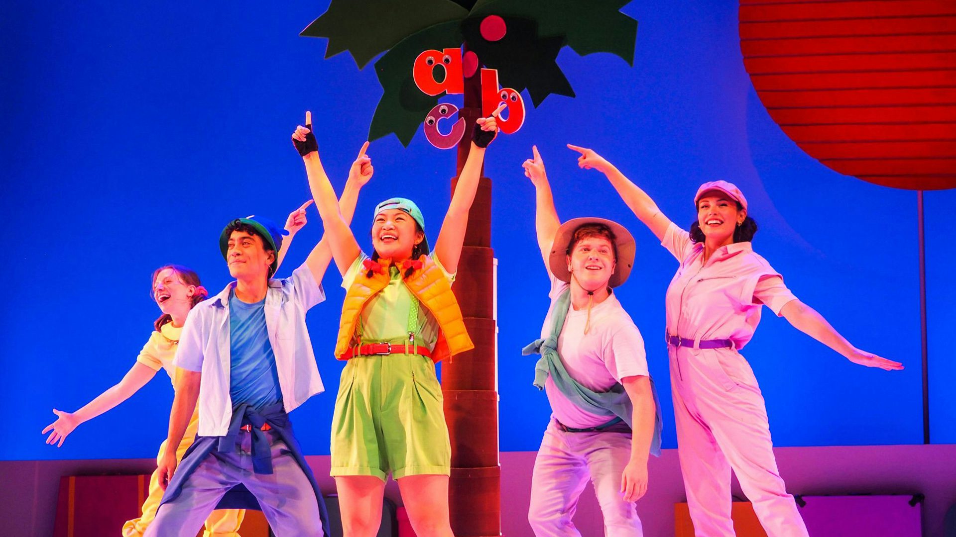 Lowercase letters "a," "b" and "c" climb to the top of the coconut tree. Five performers wearing colorful clothing smile and point up at the letters.